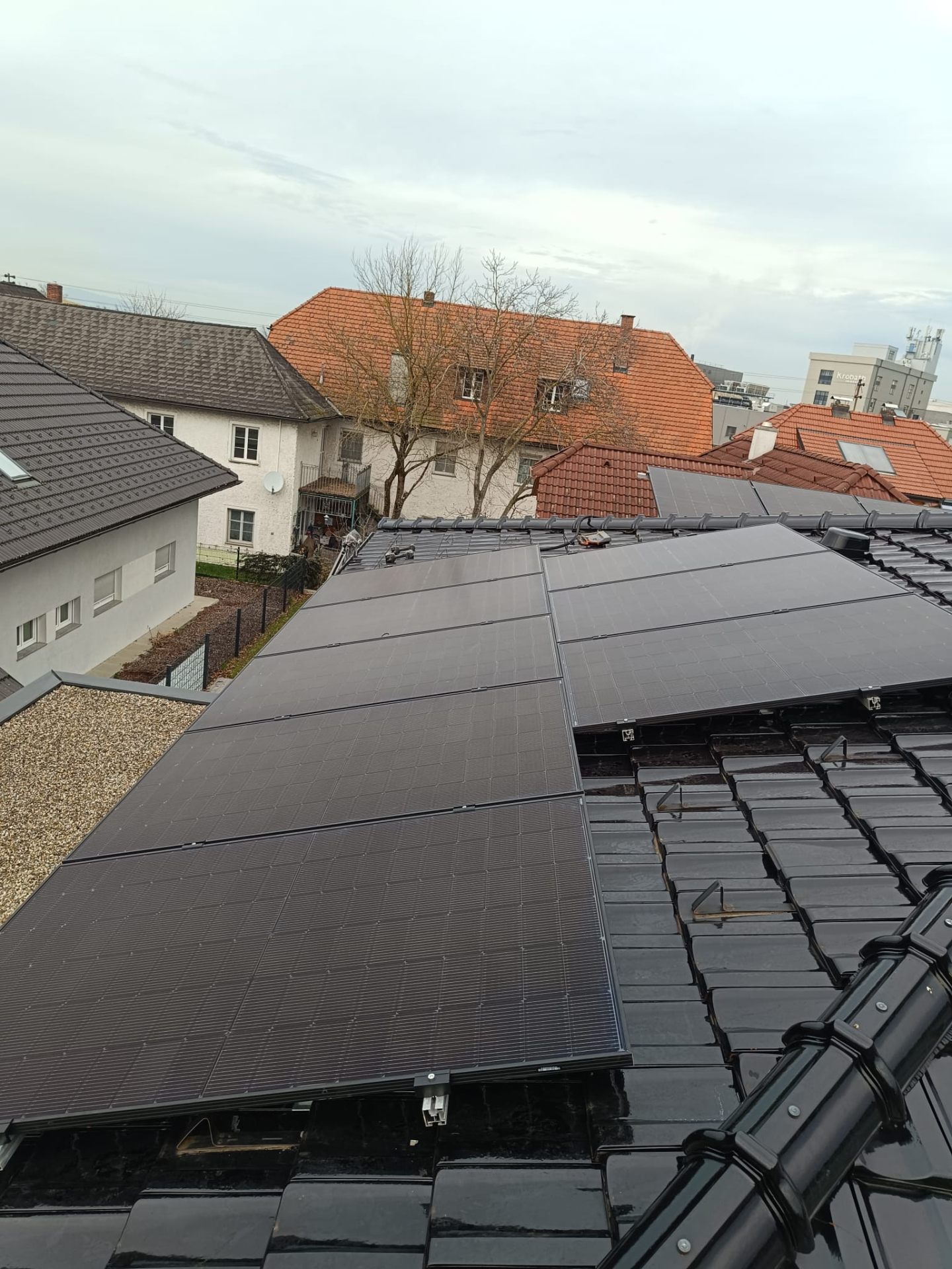 Photovoltaik-Modulreihen auf einem schwarzen Ziegeldach in einer Wohnsiedlung