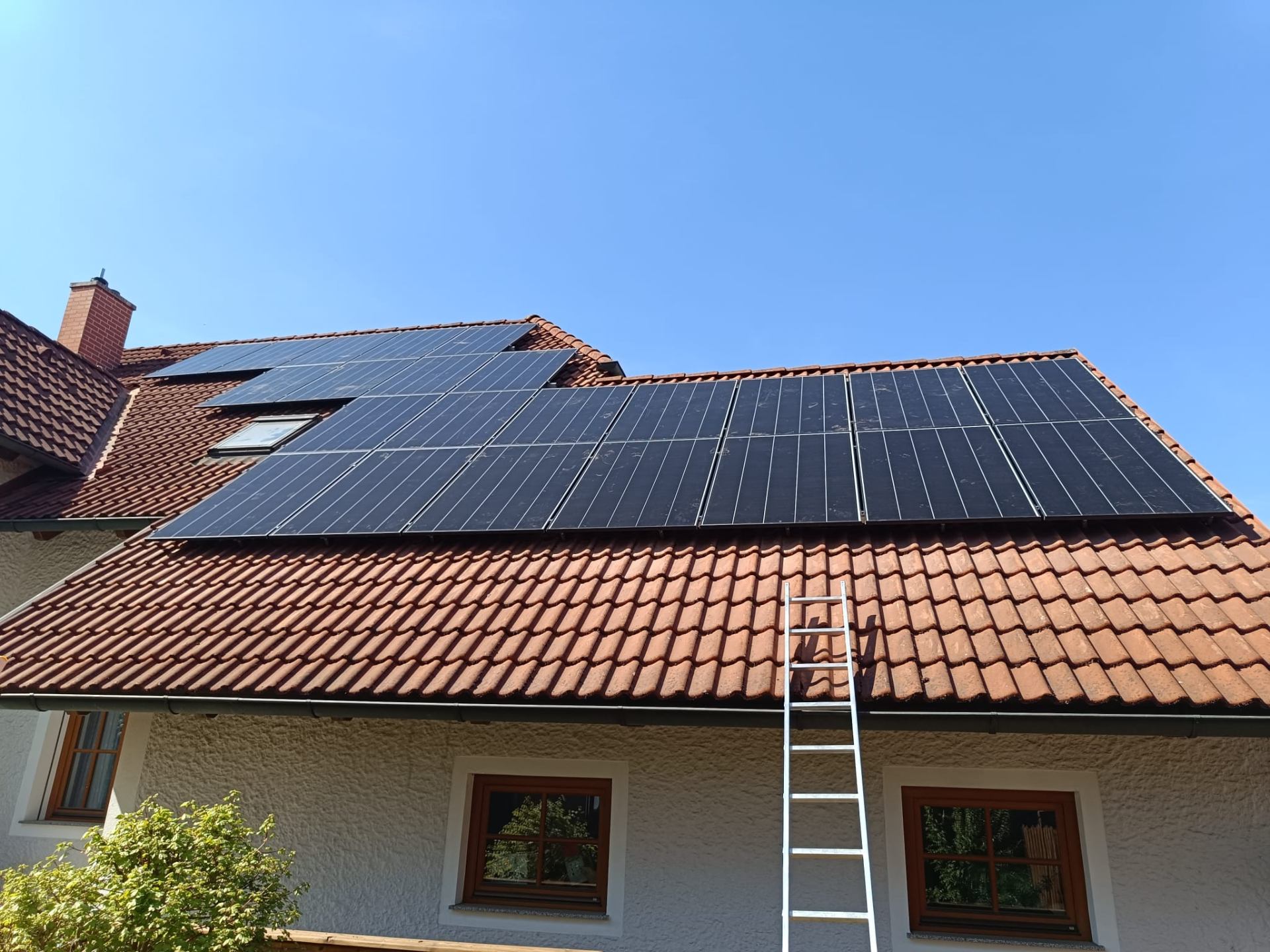 Photovoltaik-Anlage mit Full-Black-Modulen rund um ein Dachfenster auf einem roten Ziegeldach