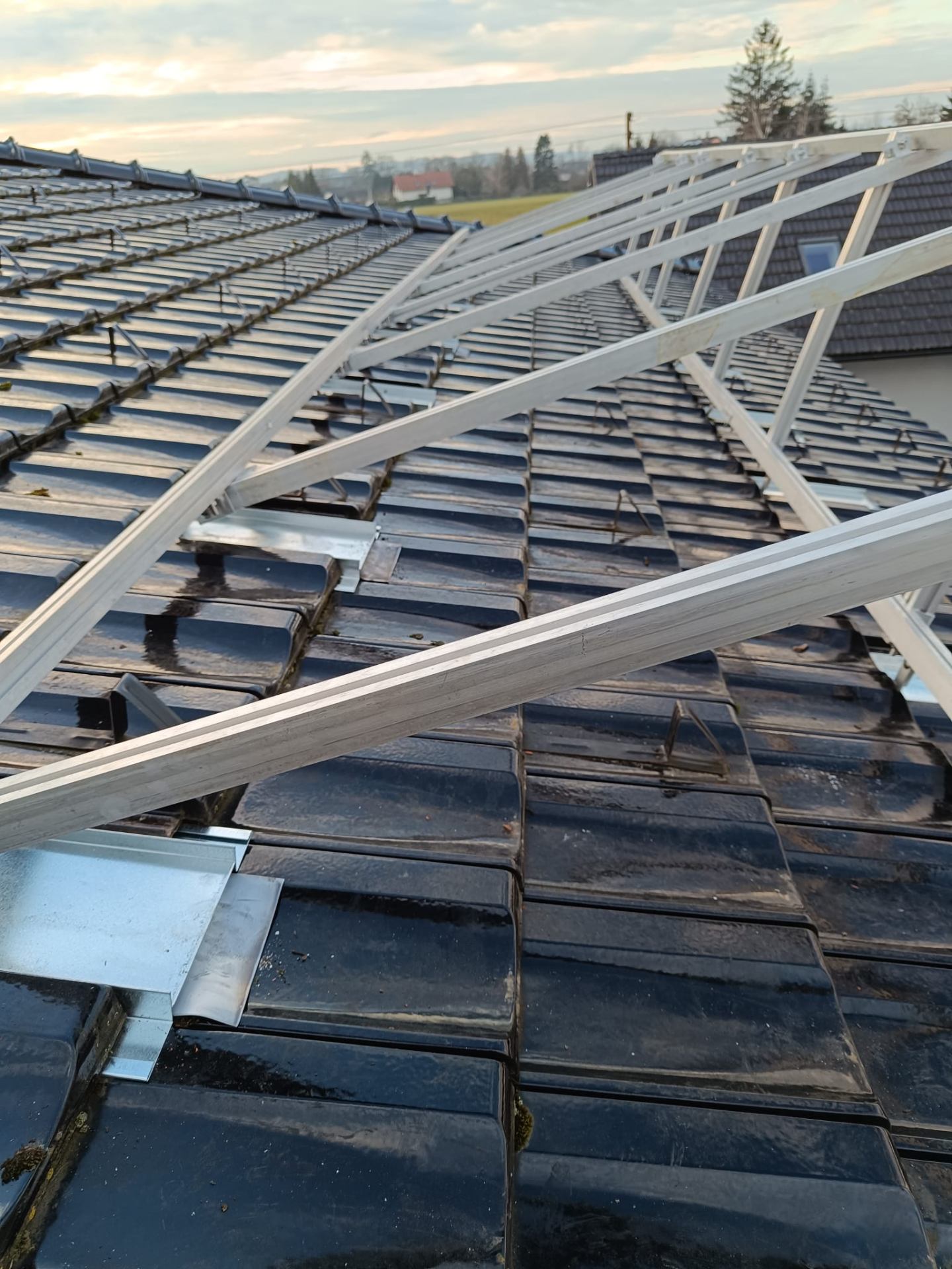 Aluminium-Unterkonstruktion einer Photovoltaik-Anlage auf einem schwarzen Ziegeldach im Sonnenuntergang