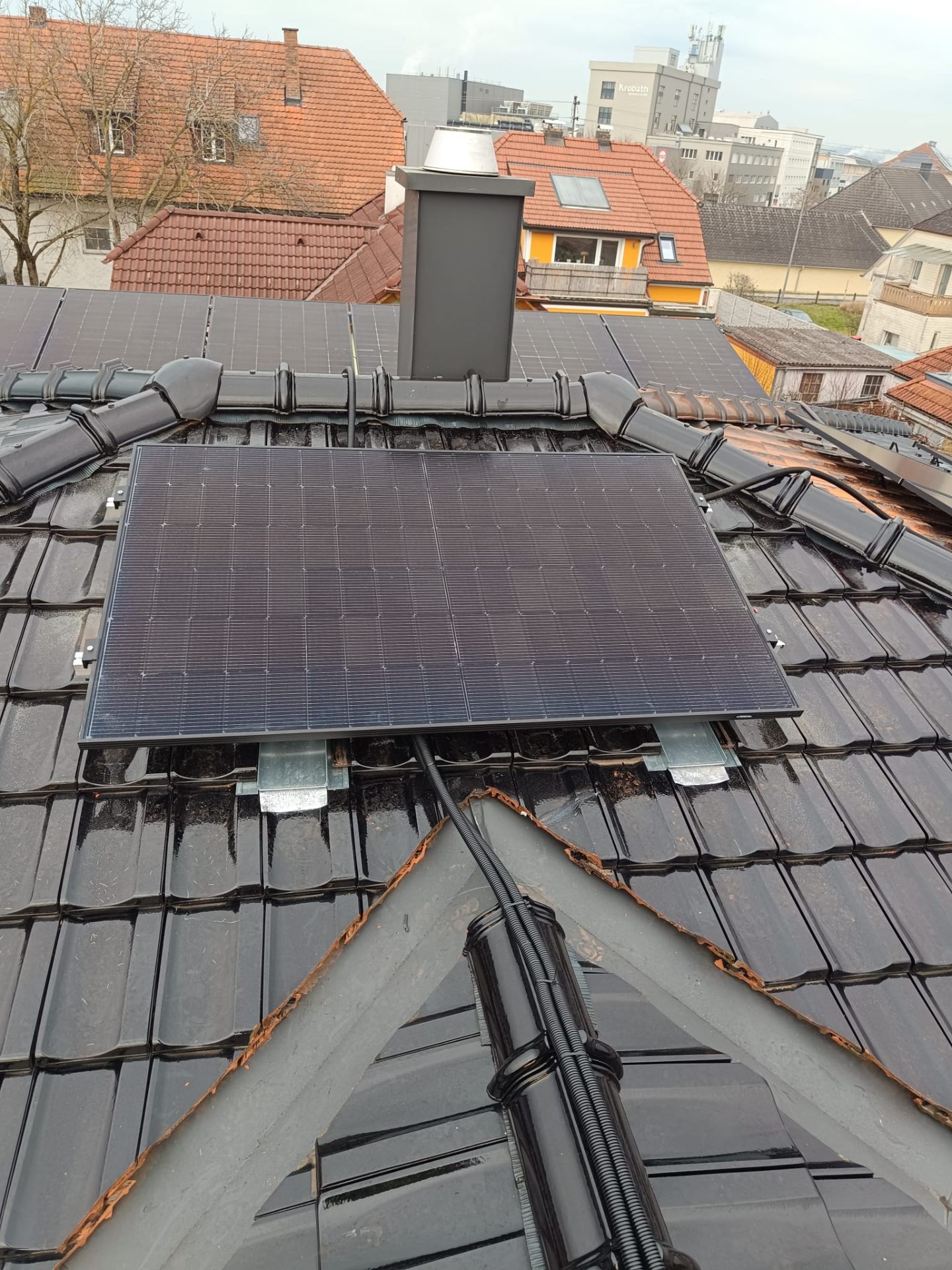 Photovoltaik-Modul präzise um Kamin und Dachgrat auf einem schwarzen Ziegeldach montiert