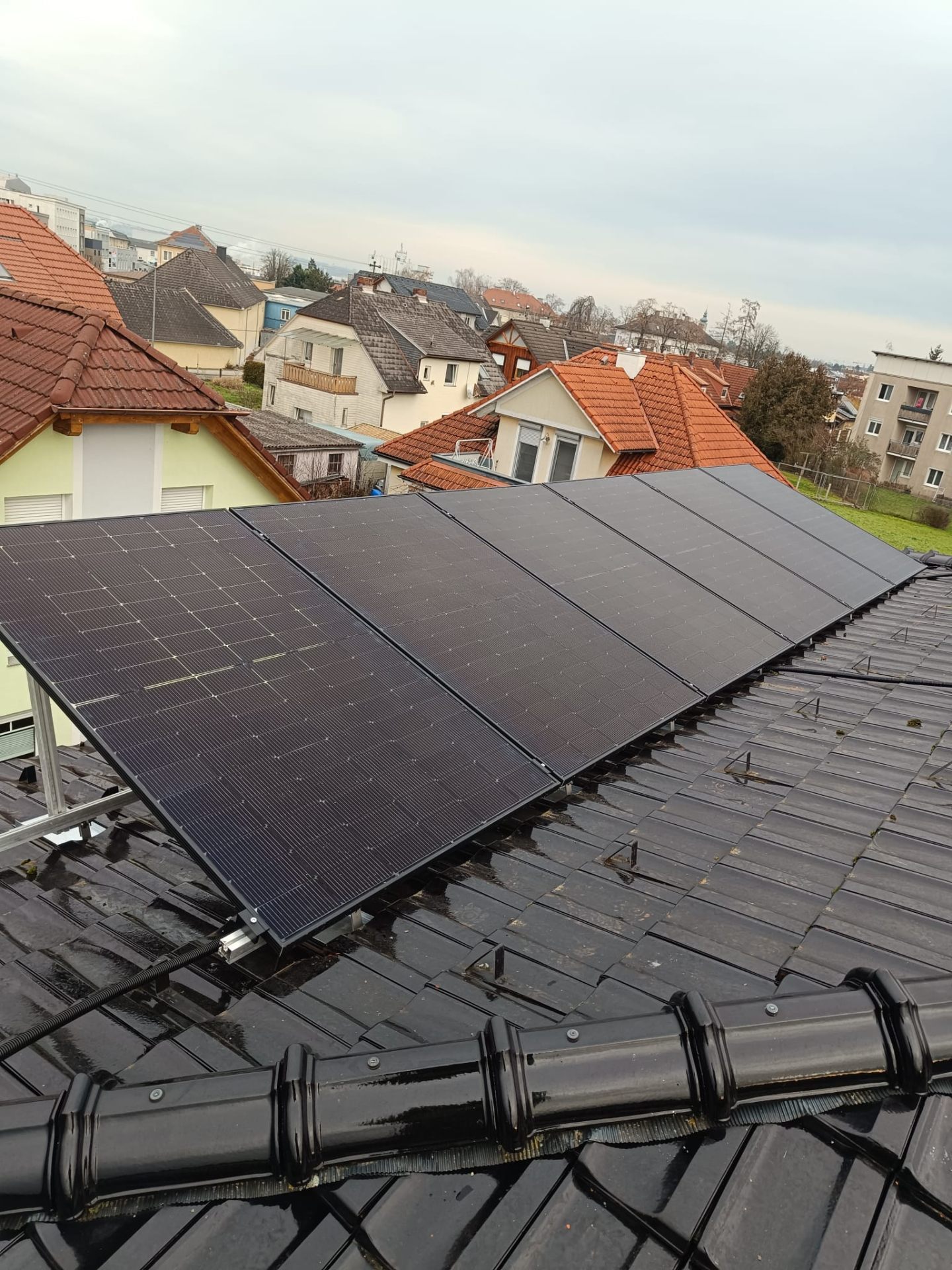 Photovoltaik-Anlage auf einem schwarzen Ziegeldach mit Blick über die Dächer der Stadt